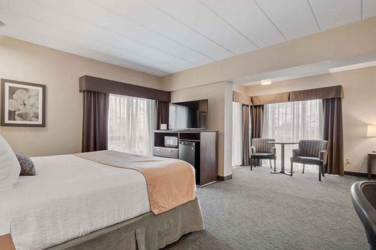 A hotel room with a large bed, a desk with a TV, a small table with chairs, and a window with curtains.