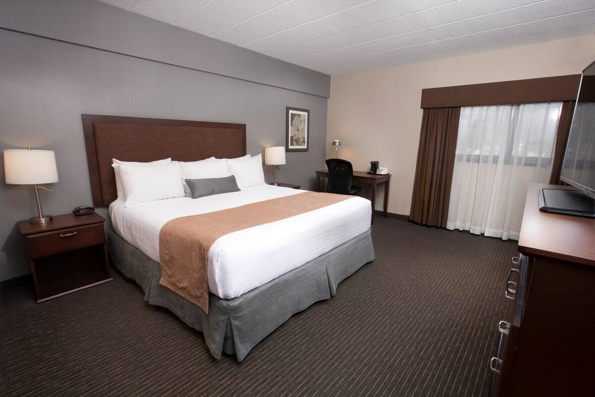 A hotel room with a large bed, two bedside tables with lamps, a desk with a chair, and a television on a dresser.