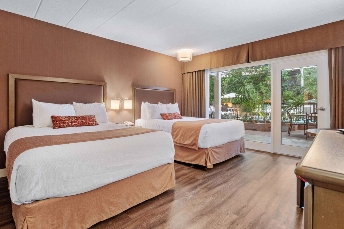 A hotel room with two beds, a large window, and a view of the outdoors.