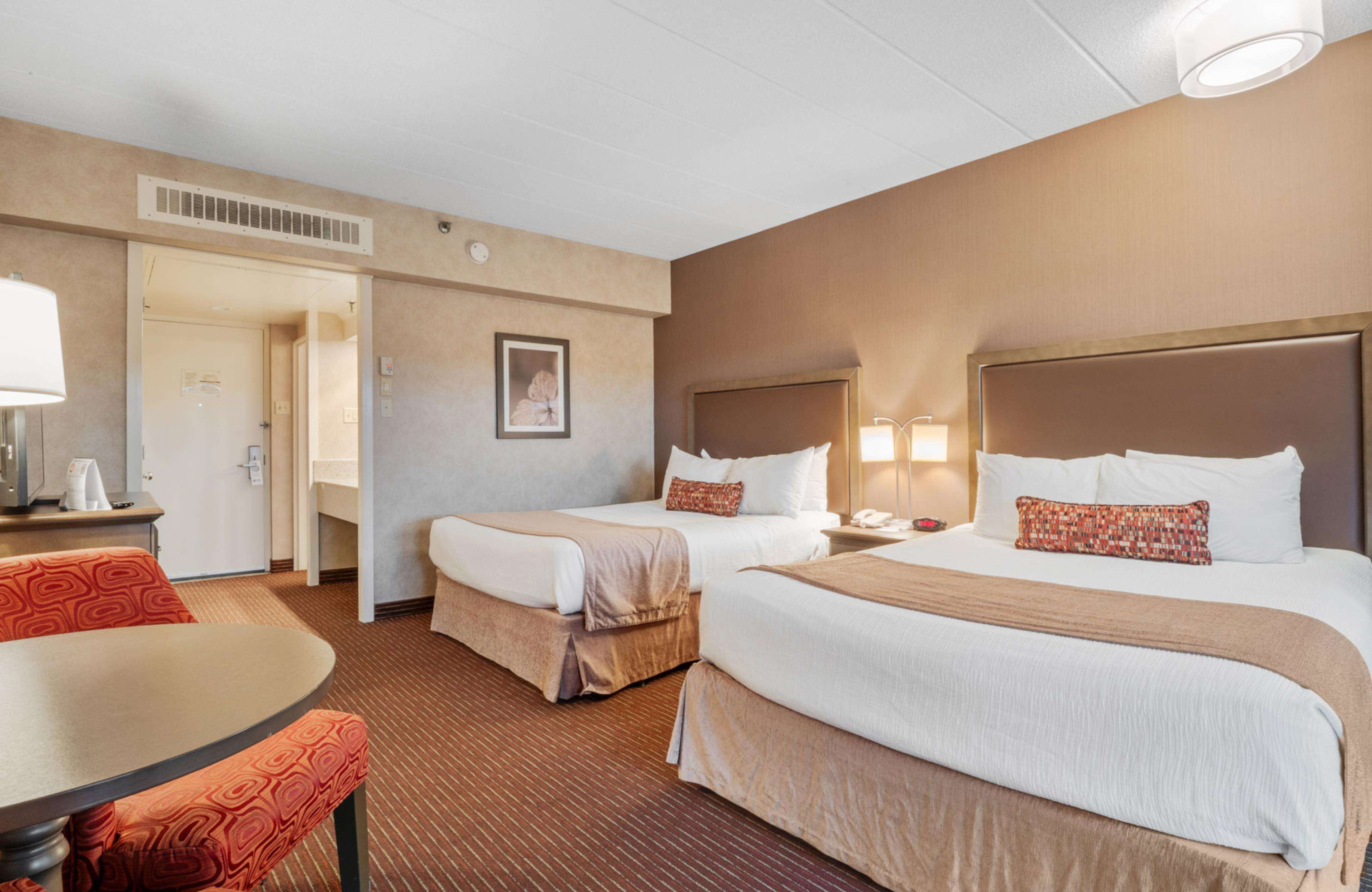 A hotel room with two beds, a desk, a chair, and a door leading to a bathroom.