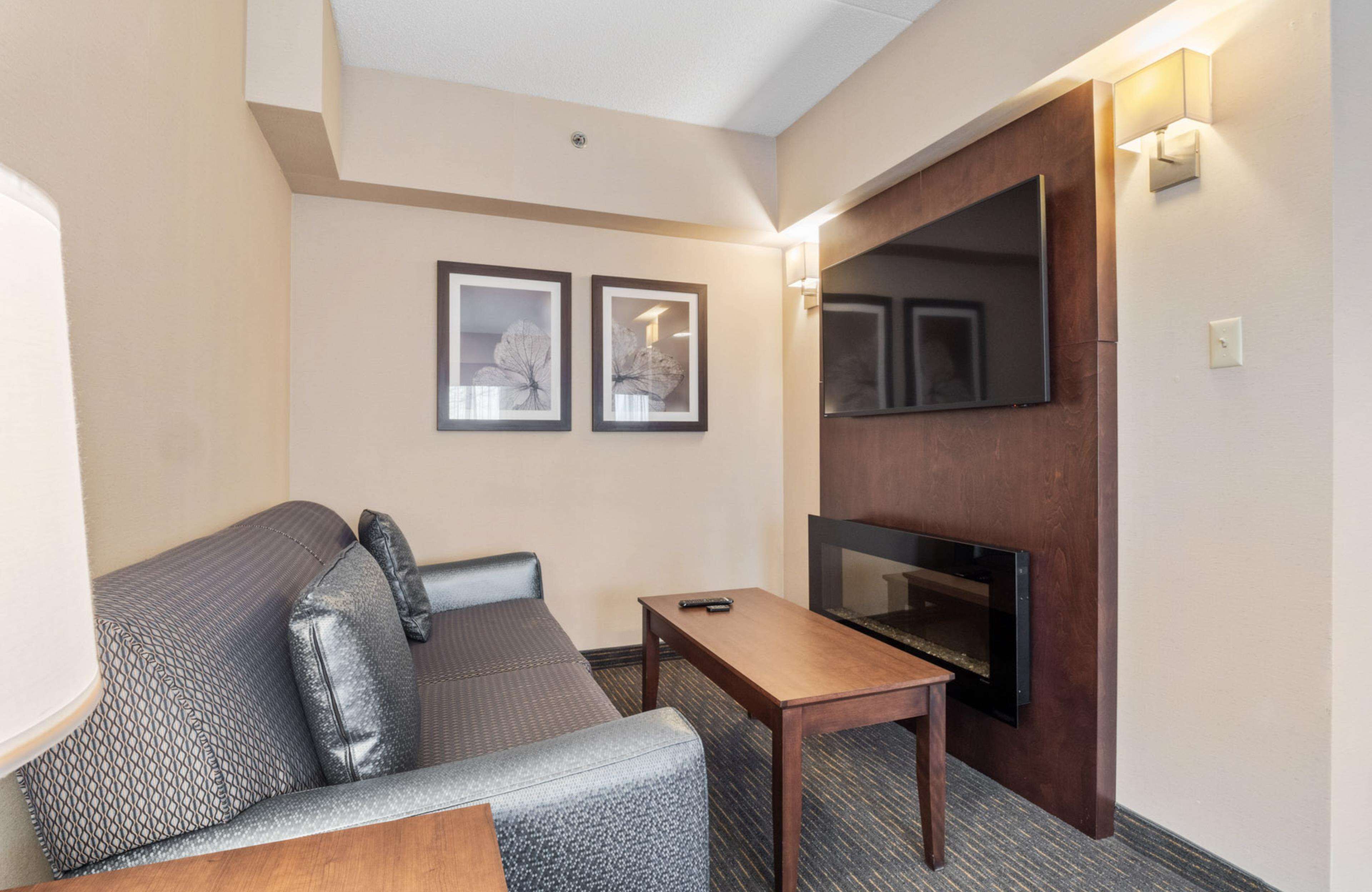 Une chambre d’hôtel équipée d’un canapé, d’une petite table, d’un téléviseur à écran plat fixé sur un panneau en bois, et de deux tableaux encadrés accrochés au mur.