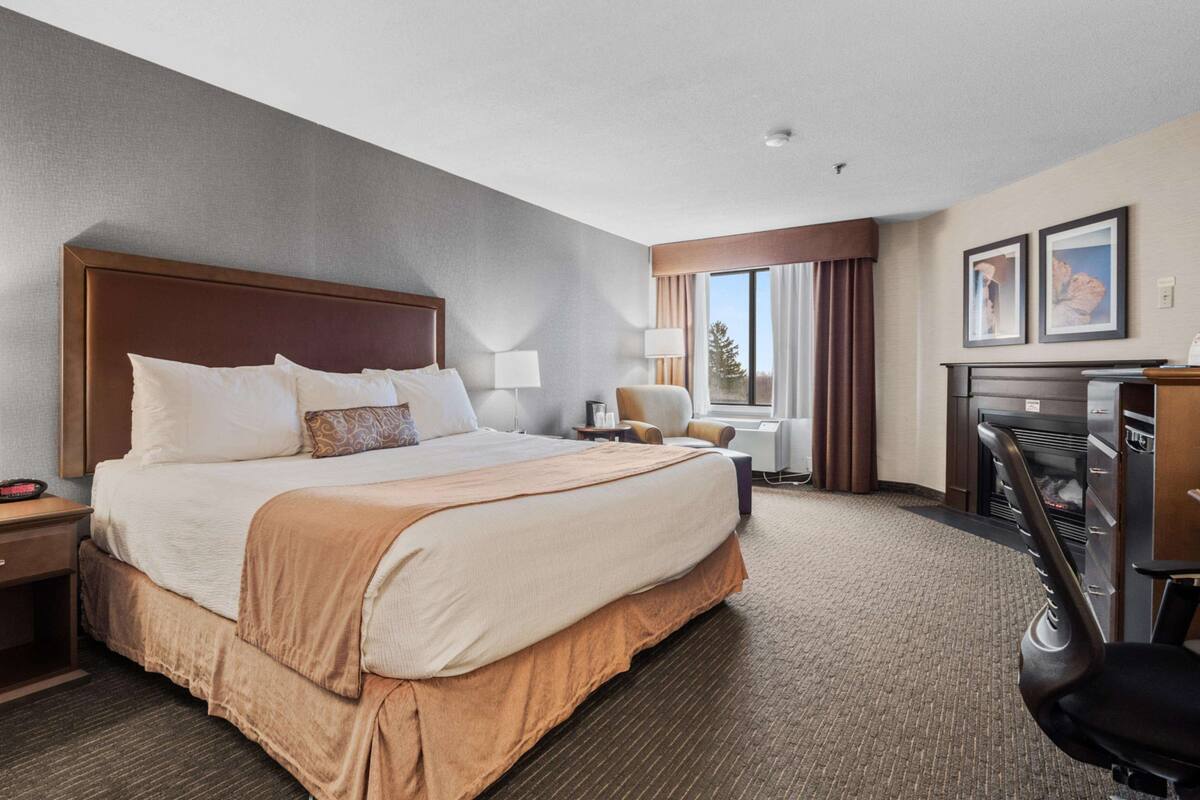 A hotel room with a large bed, a desk with a computer, a chair, and a window with curtains.