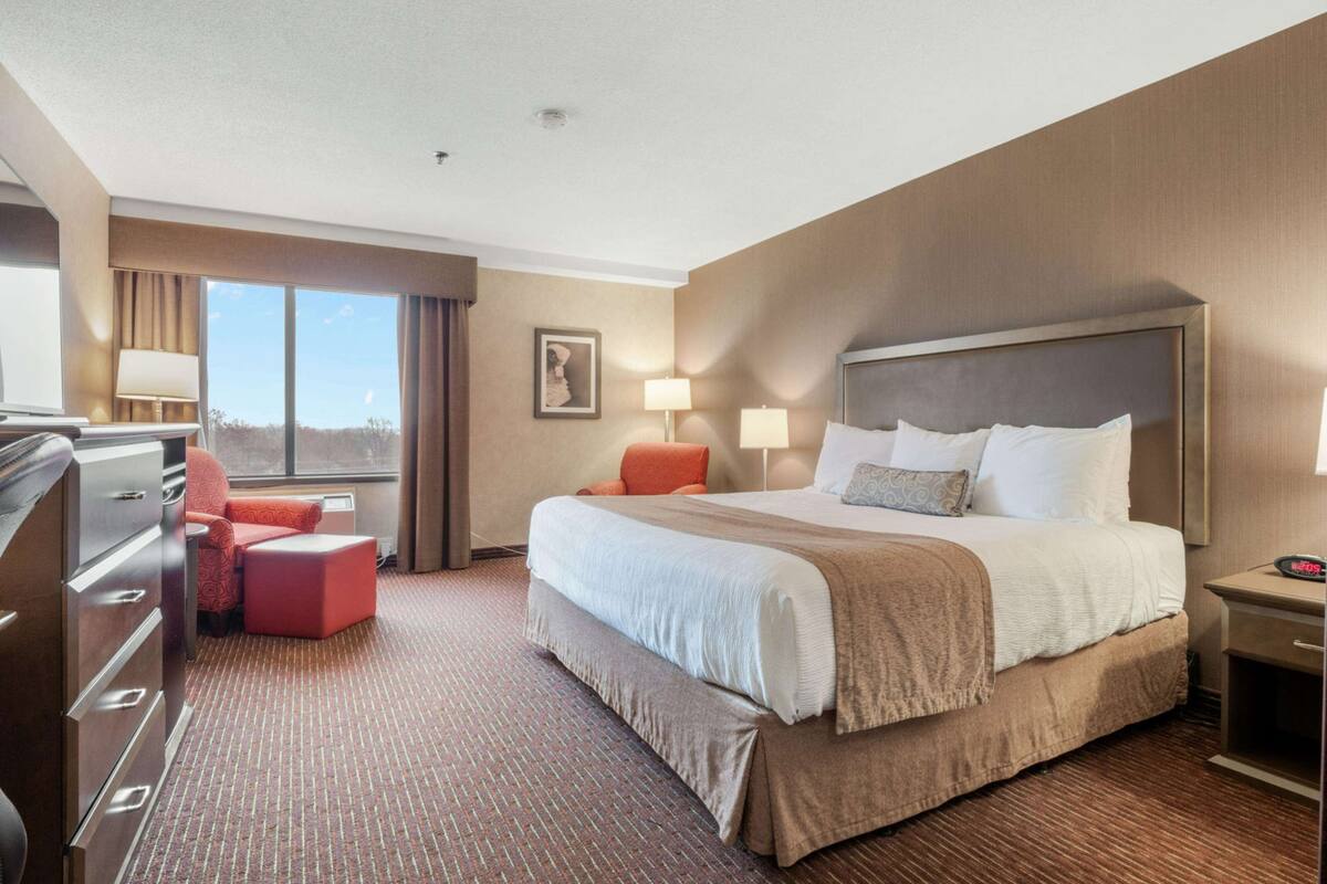 A hotel room with a large bed, a desk, a chair, and a dresser.