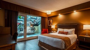 A hotel room with a large bed, a desk, a chair, a nightstand, and a view of a balcony with a staircase. - Best Western Plus Cairn Croft Hotel (Niagara Falls)