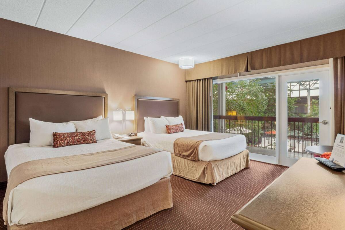 A hotel room with two beds, a desk, and a balcony with a view.