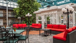 An indoor patio area with wicker furniture, red cushions, and a white lattice structure. - Best Western Plus Cairn Croft Hotel (Niagara Falls)