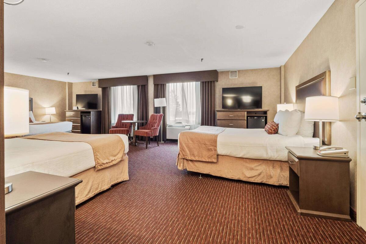 A hotel room with two beds, a desk, a chair, a TV, and a window with curtains.