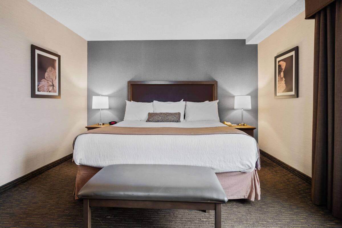 A hotel room with a large bed, two bedside tables, a bench, and two wall-mounted lamps.