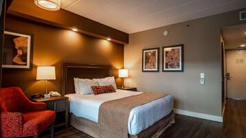 A hotel room with a bed, two bedside lamps, a red chair, and two framed pictures on the wall.