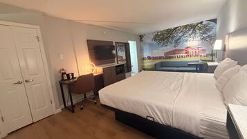 A hotel room with a bed, desk, chair, TV, and a mural on the wall.