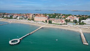 An aerial view of a coastal city with a prominent waterfront promenade, a large hotel with a red facade, and a pier extending into the water. - Ambasciatori Hotel Mestre Venice, Tapestry Collection by Hilton (Mestre)