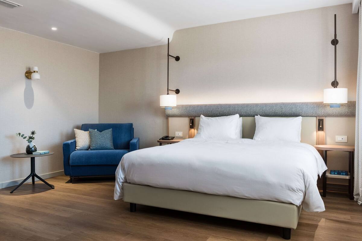 A hotel room with a large bed, a blue sofa, a small side table, and two wall-mounted lamps.