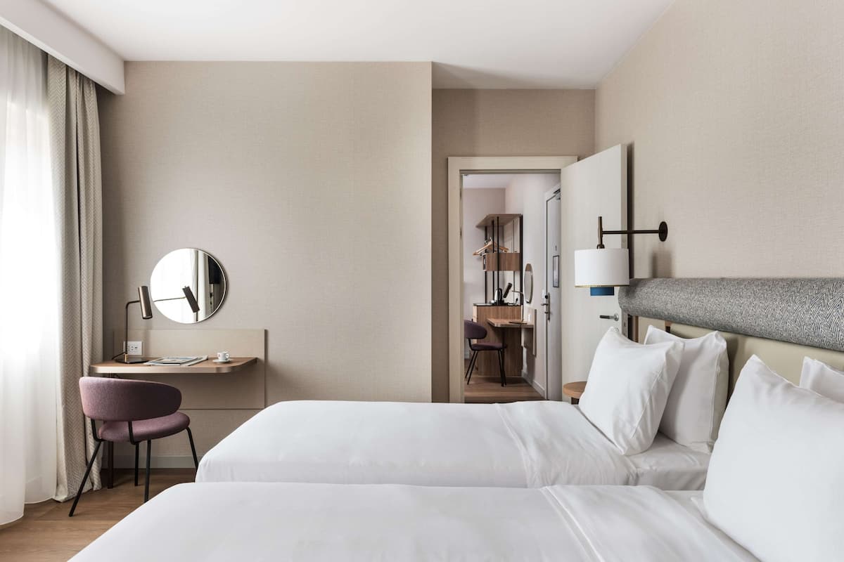 A hotel room with two beds, a desk, a chair, a mirror, and a wardrobe.