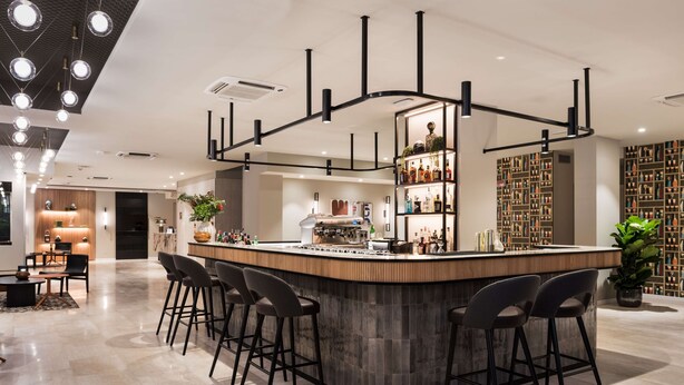 A modern bar area with a curved counter, bar stools, and a decorative ceiling light fixture. - Ambasciatori Hotel Mestre Venice, Tapestry Collection by Hilton (Mestre)