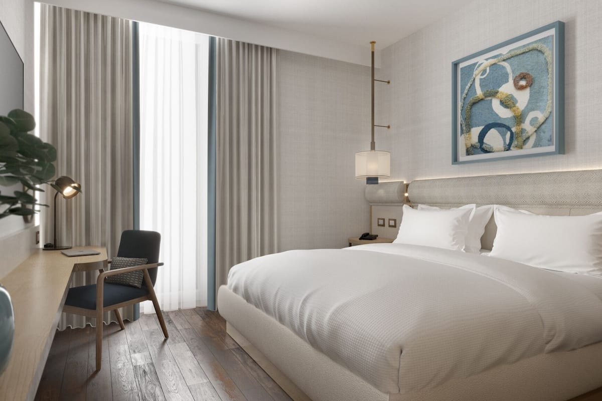 A hotel room with a large bed, a desk with a chair, a lamp, and a painting on the wall.