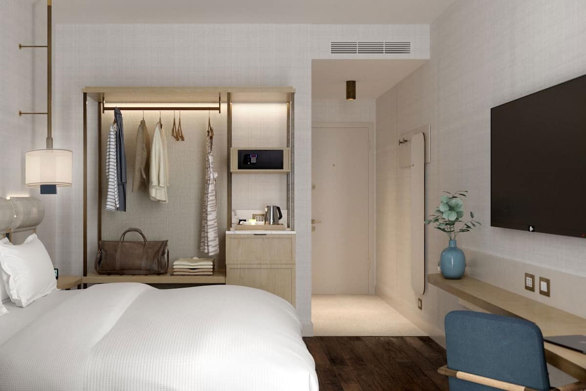 A hotel room with a bed, a desk with a chair, a TV, a wardrobe, and a bathroom.