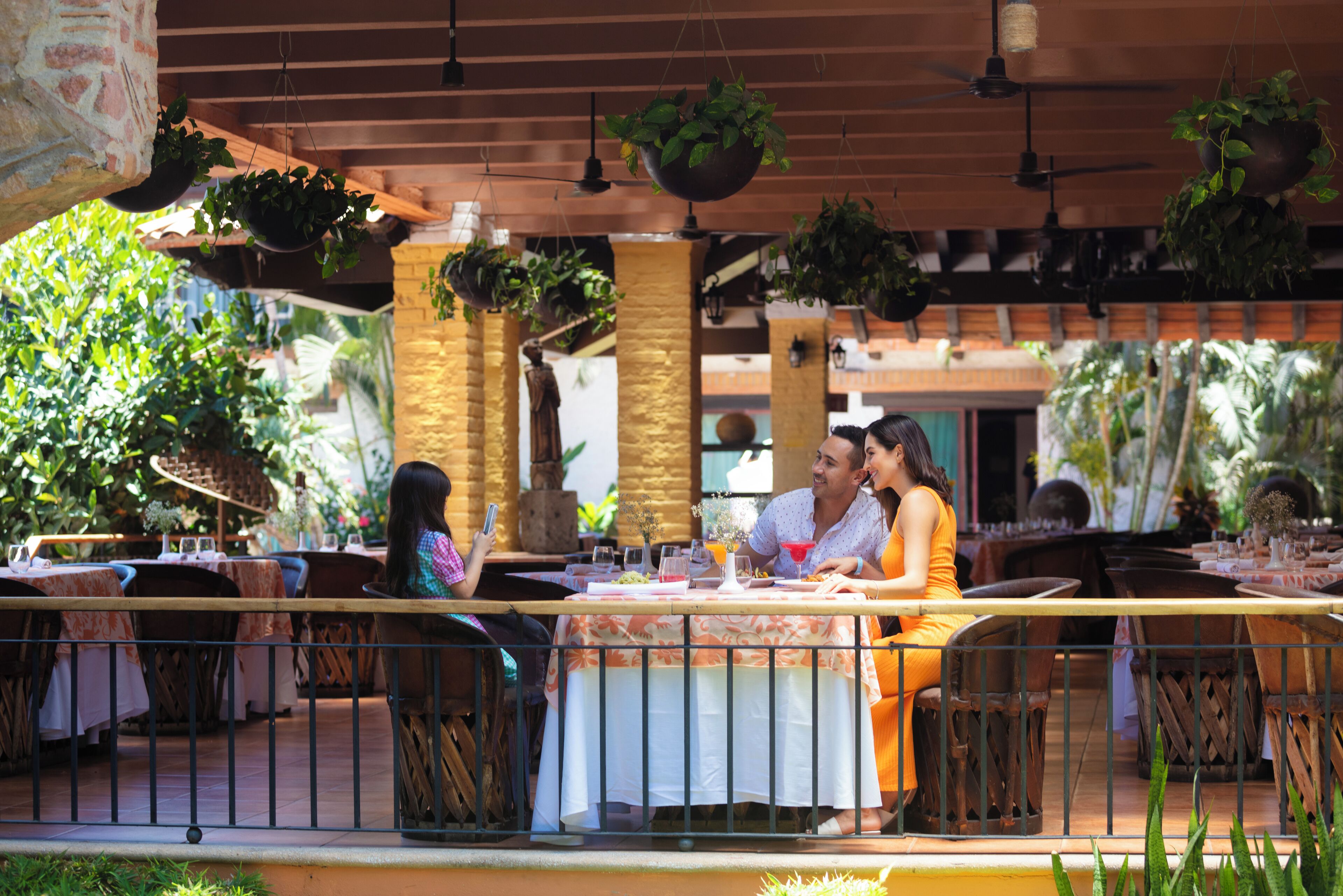 An outdoor dining area with tables and chairs, surrounded by hanging plants and a brick wall.