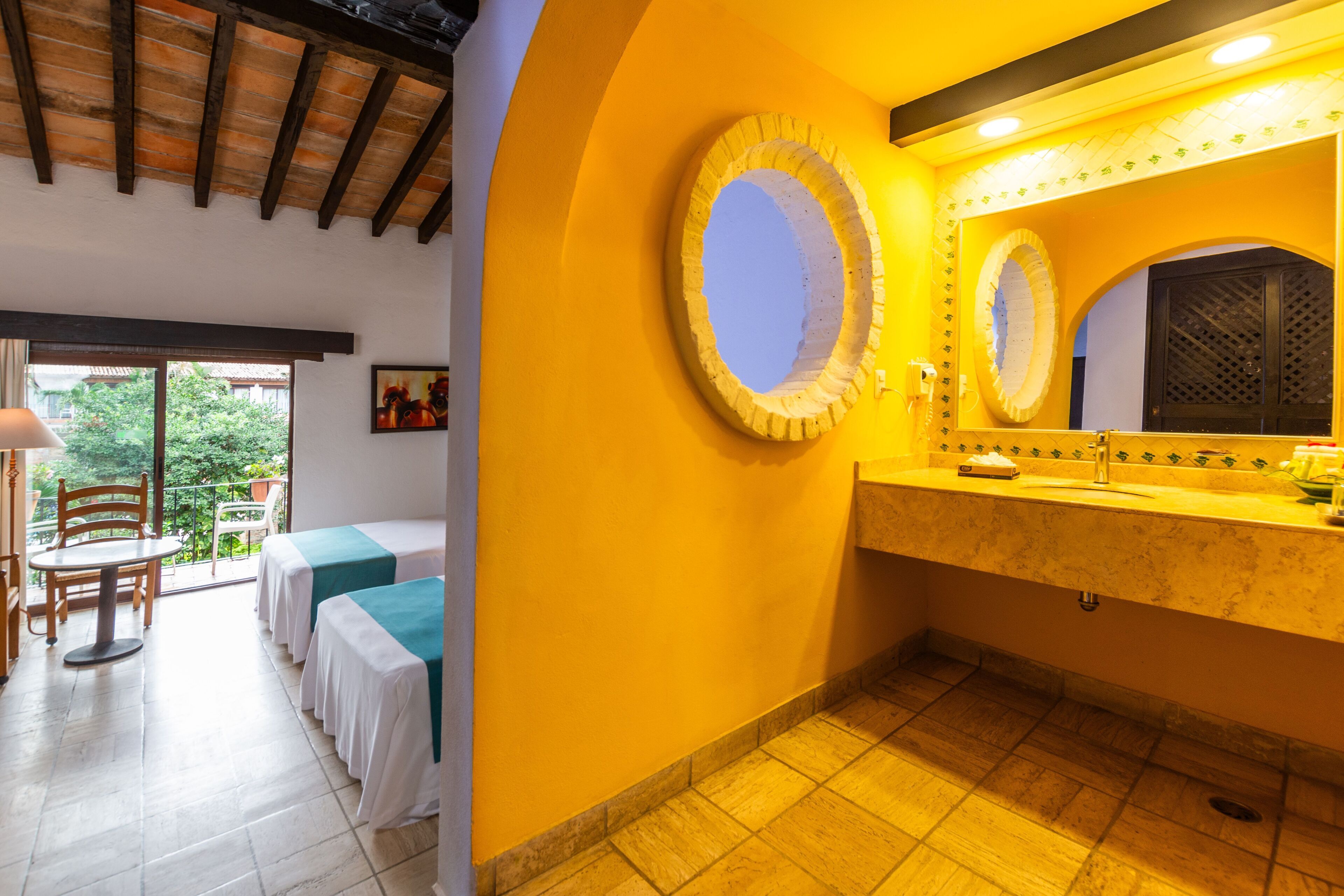 A hotel room with a balcony, a bathroom with a large mirror, and a table with chairs.