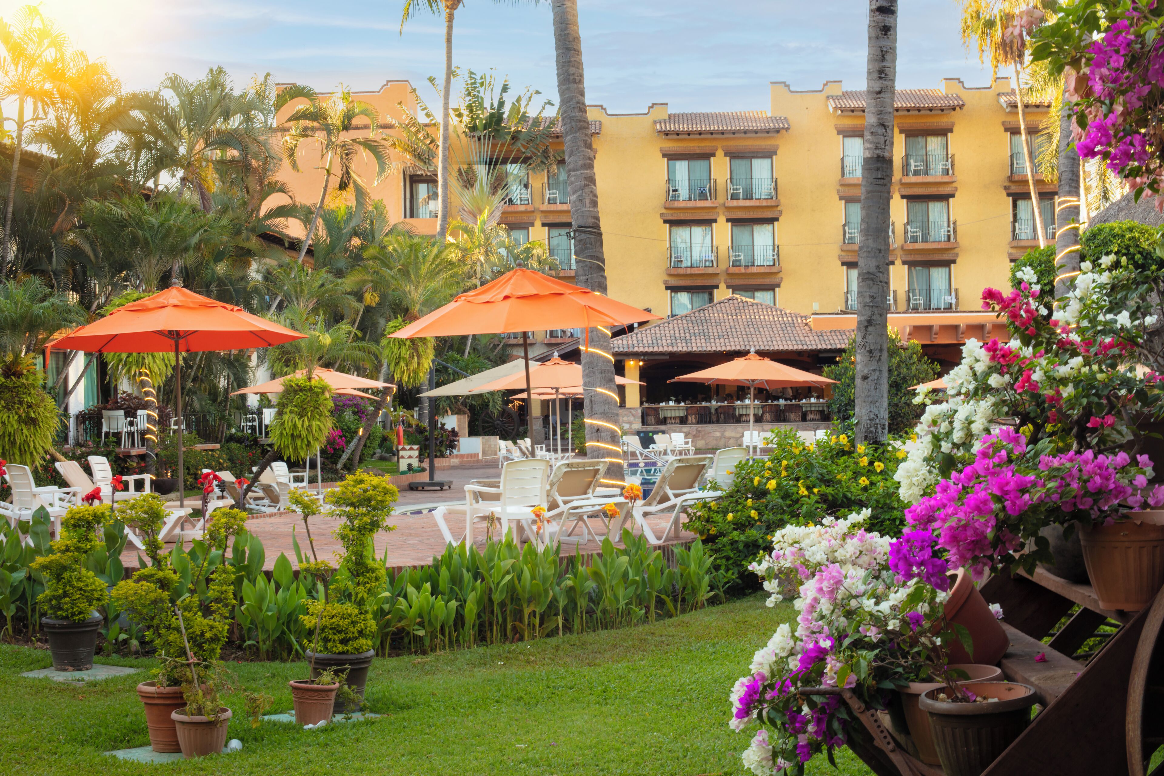 Un patio de hotel con mesas al aire libre, palmeras y un edificio con balcones.
