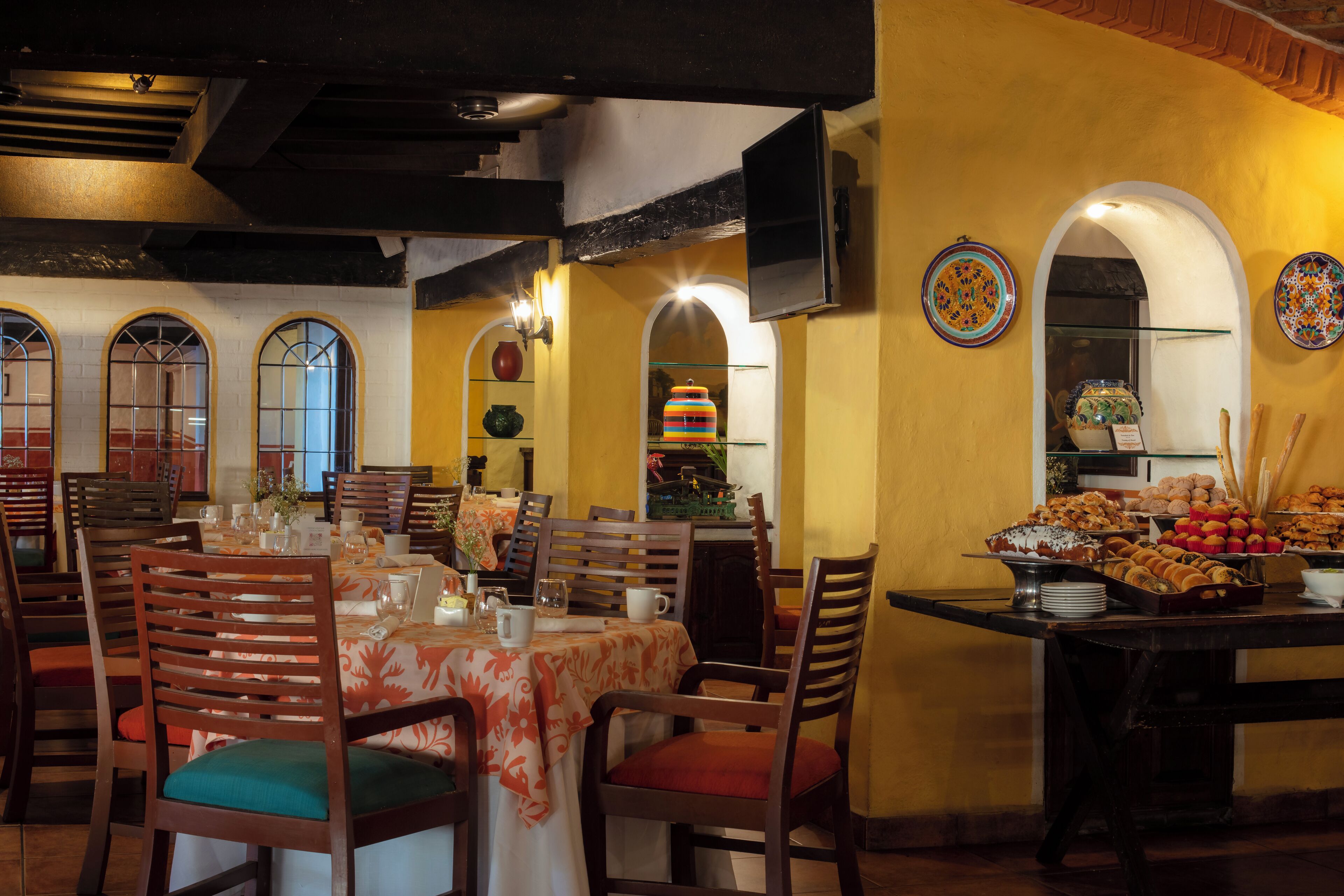 Un comedor con mesas dispuestas para una comida, sillas de madera y una mesa de buffet con distintos alimentos.