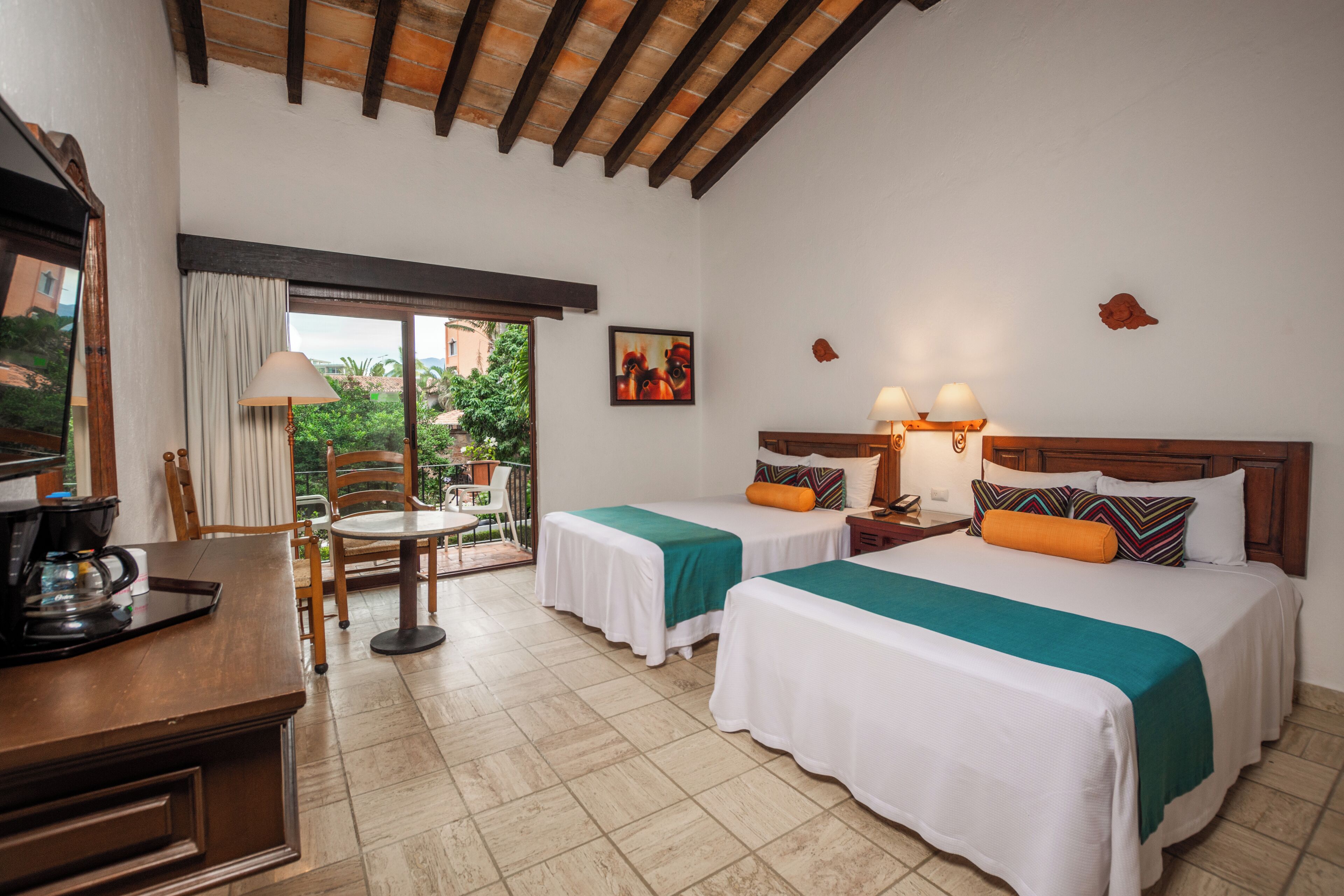 A hotel room with two beds, a dining area, and a view of the outdoors.