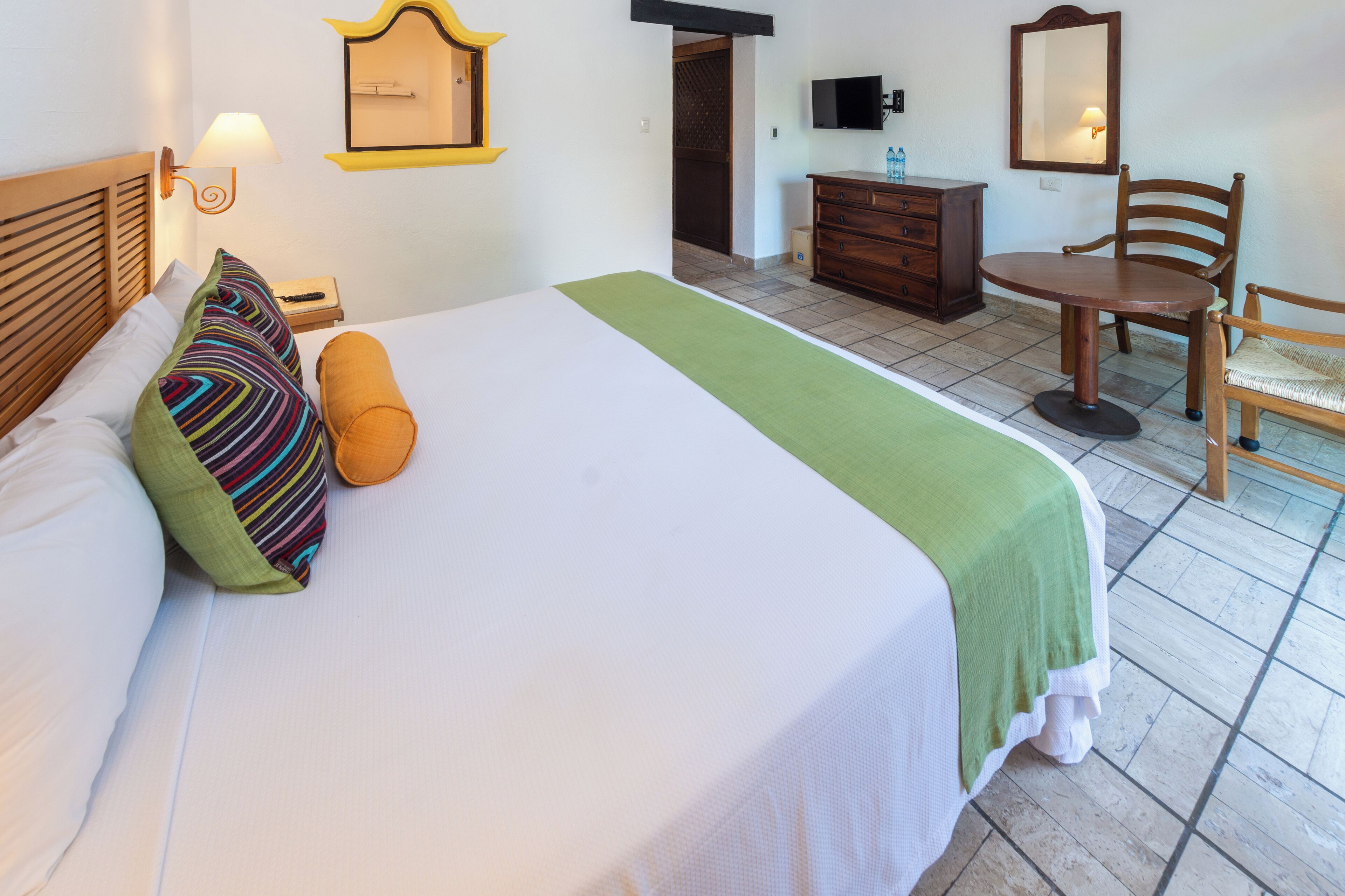 A hotel room with a large bed, a wooden dresser, a chair, and a television on a dresser.