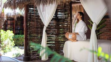 Relax in a tranquil retreat with a bed under a thatched roof, surrounded by lush greenery and a brick wall.