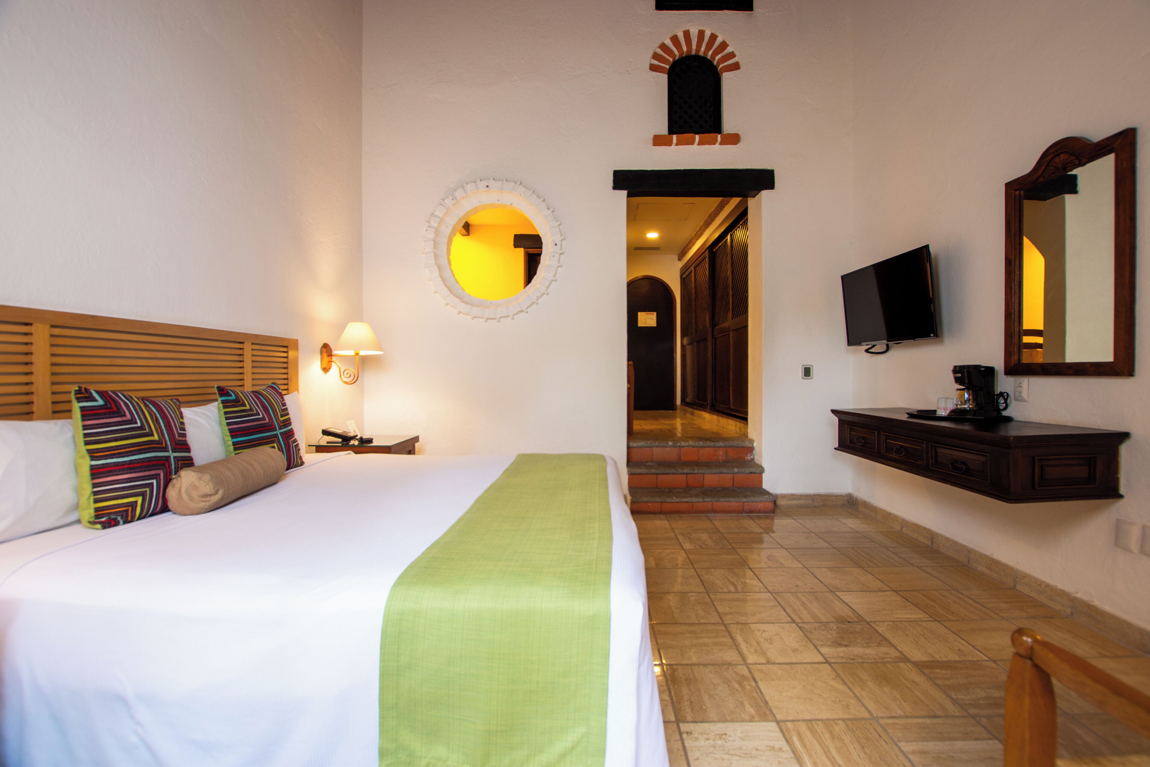 Habitación de hotel con una cama, un televisor, un espejo y una escalera que lleva a otra zona.