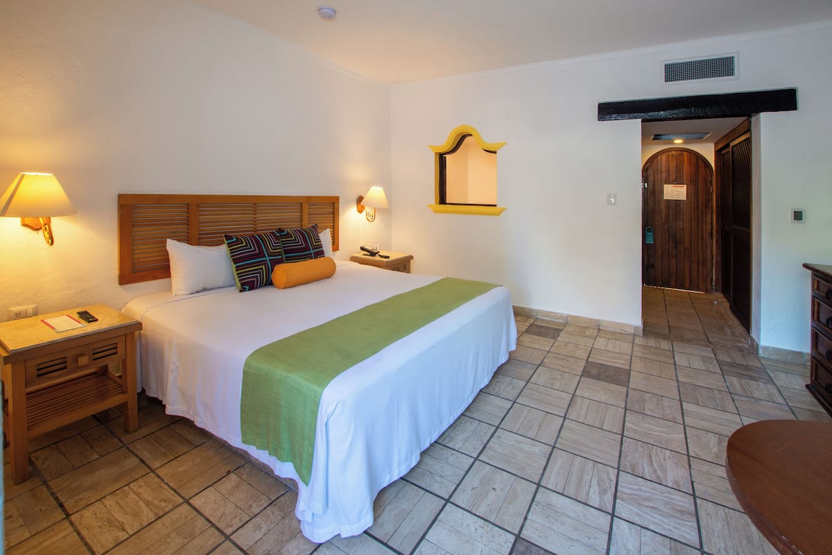 Une chambre d’hôtel comprenant un lit, des tables de chevet, une commode, un miroir et une porte donnant sur une autre pièce.