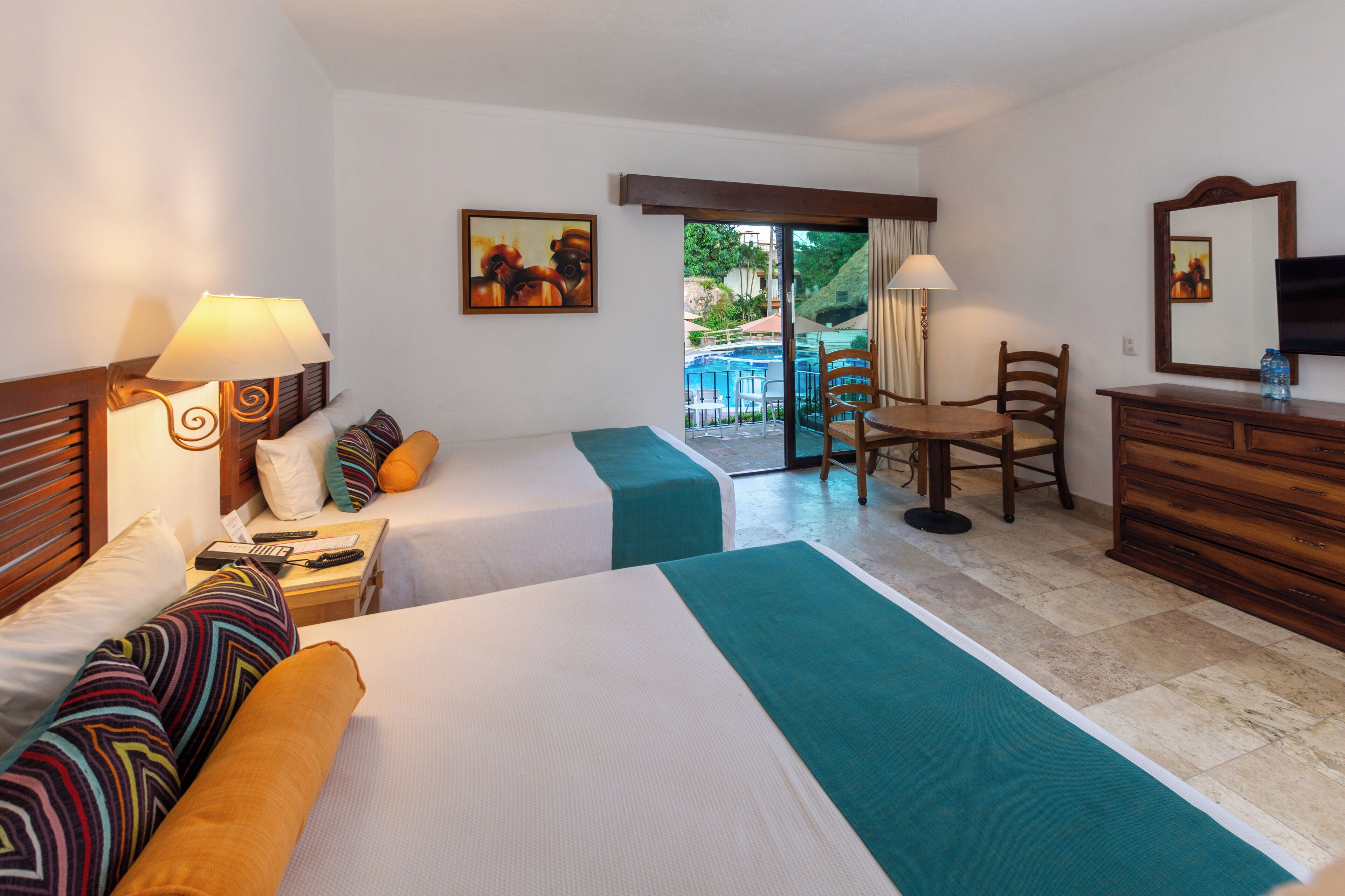 A hotel room with two beds, a desk, a chair, a TV, and a view of an outdoor pool.