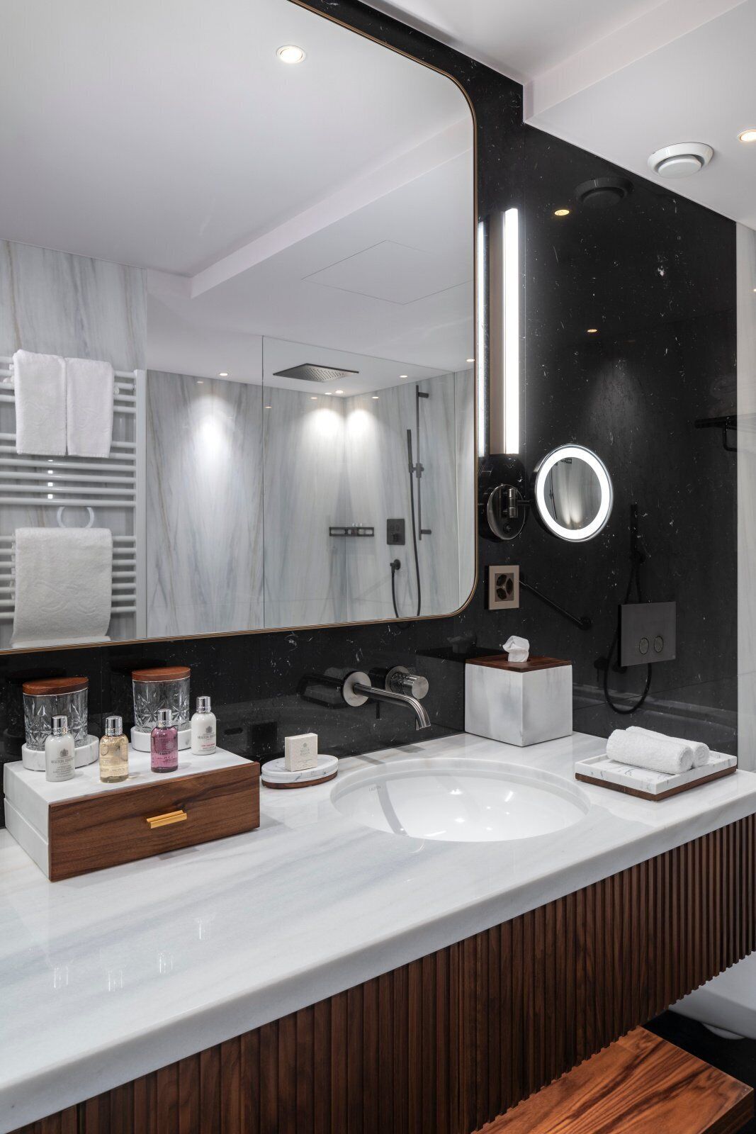 A modern bathroom with a large mirror, a round vanity mirror, and a white marble sink.
