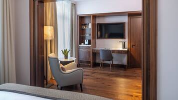A hotel room with a bed, a desk with a chair, a TV, a lamp, and a potted plant.