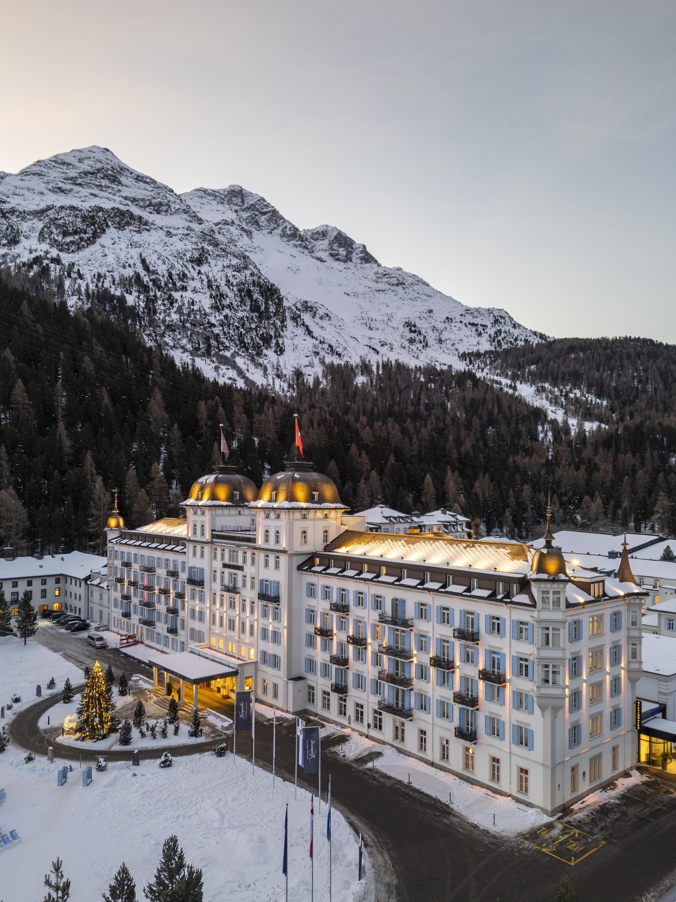 Un grande hotel a più piani con una facciata simmetrica, numerosi balconi e un cortile centrale con un albero di Natale.