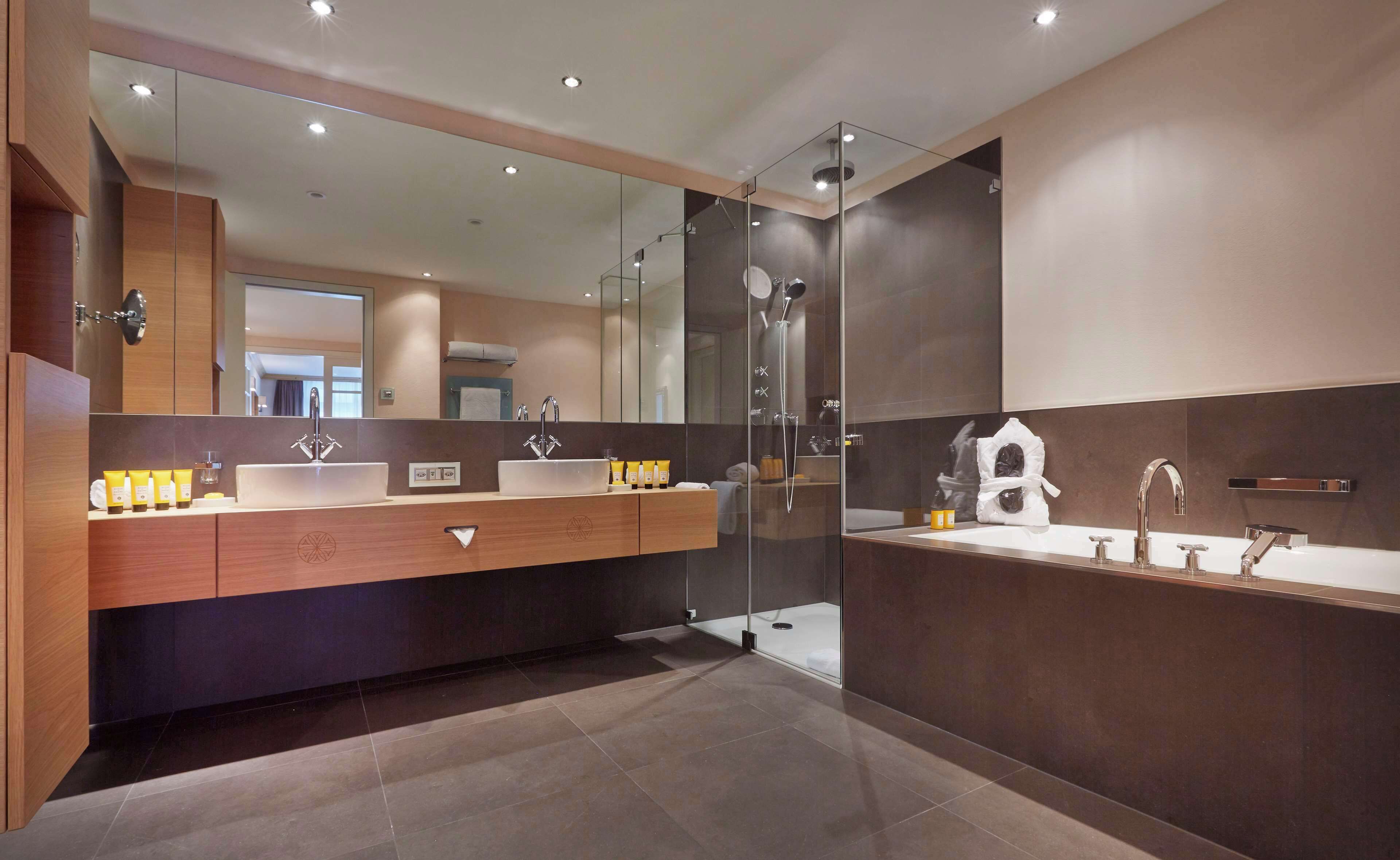 A modern bathroom with a large mirror, two sinks, and a glass-enclosed shower.