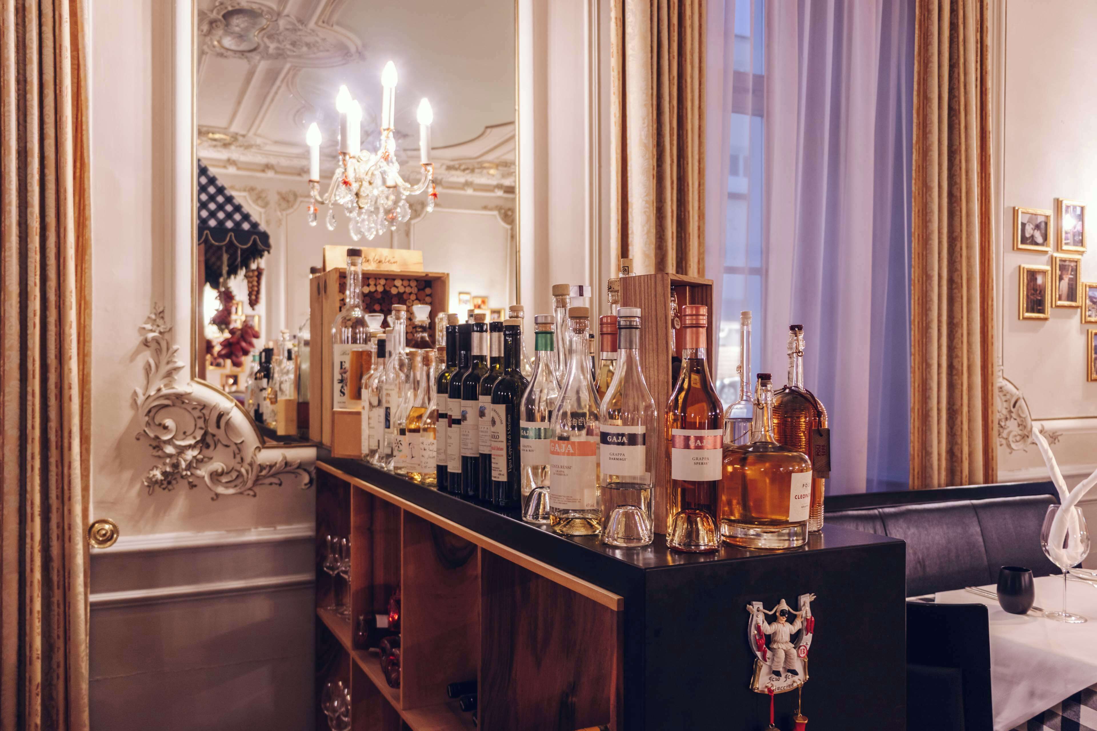 A bar area with a variety of liquor bottles, a chandelier, and a mirror reflecting the room's decor.