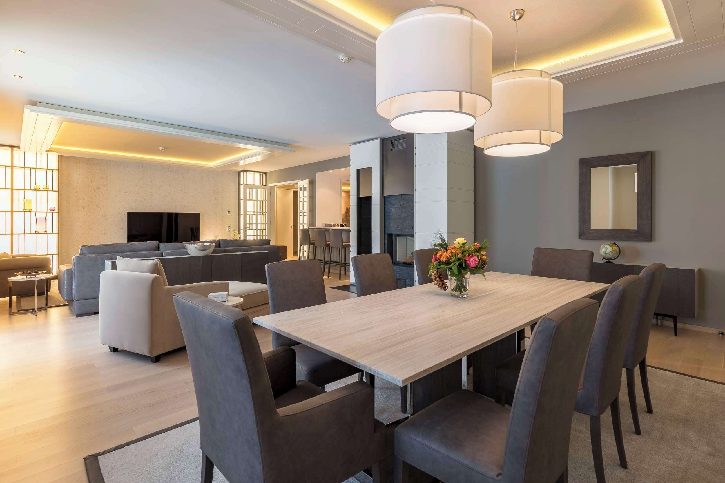 A modern living room with a dining area, grey sofas, a flat-screen TV, and a wooden dining table with chairs.