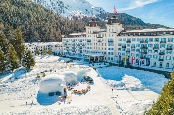 A large hotel with multiple floors, a snow-covered courtyard, and a mountain backdrop.