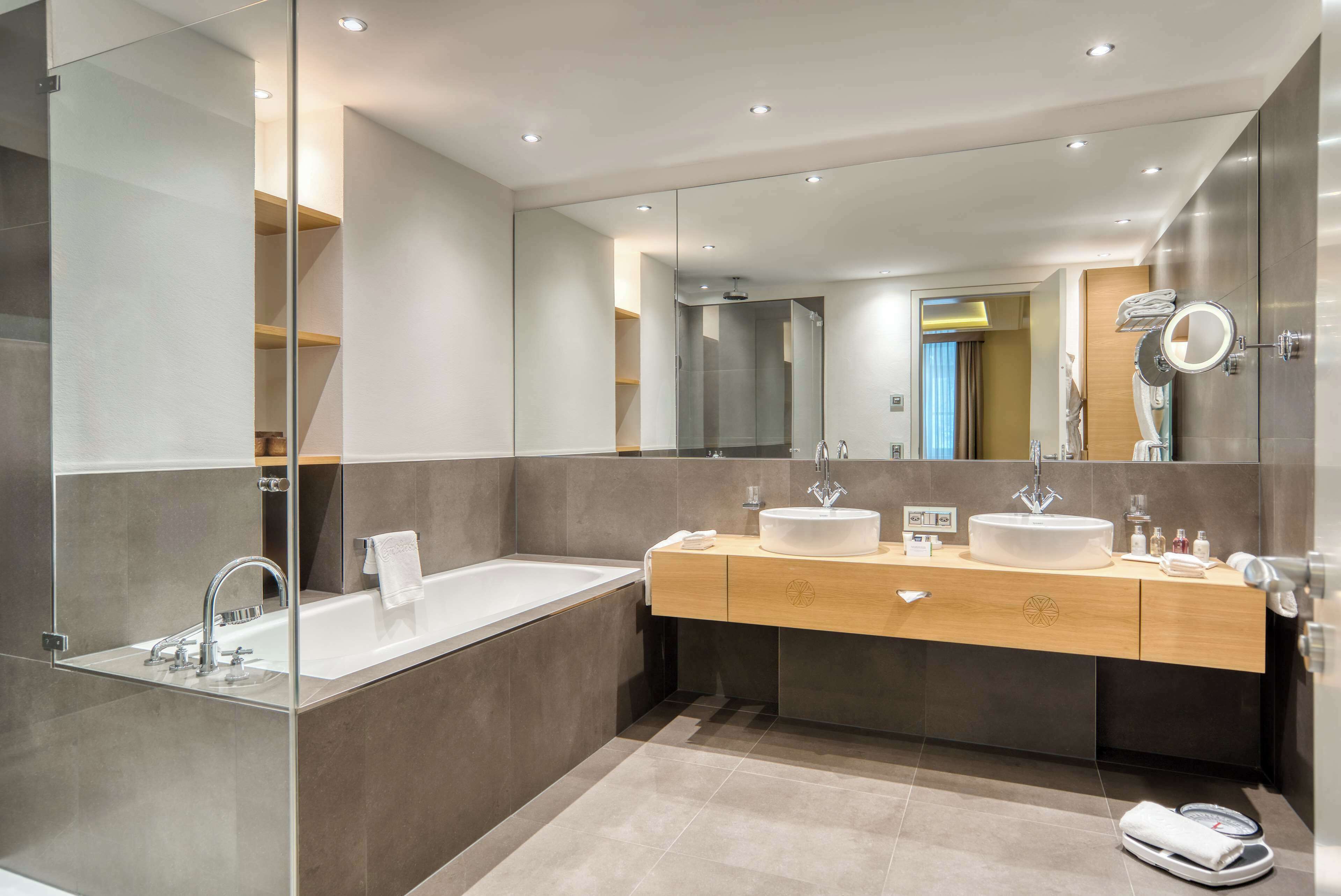 A modern bathroom with a large mirror, two sinks, and a bathtub.