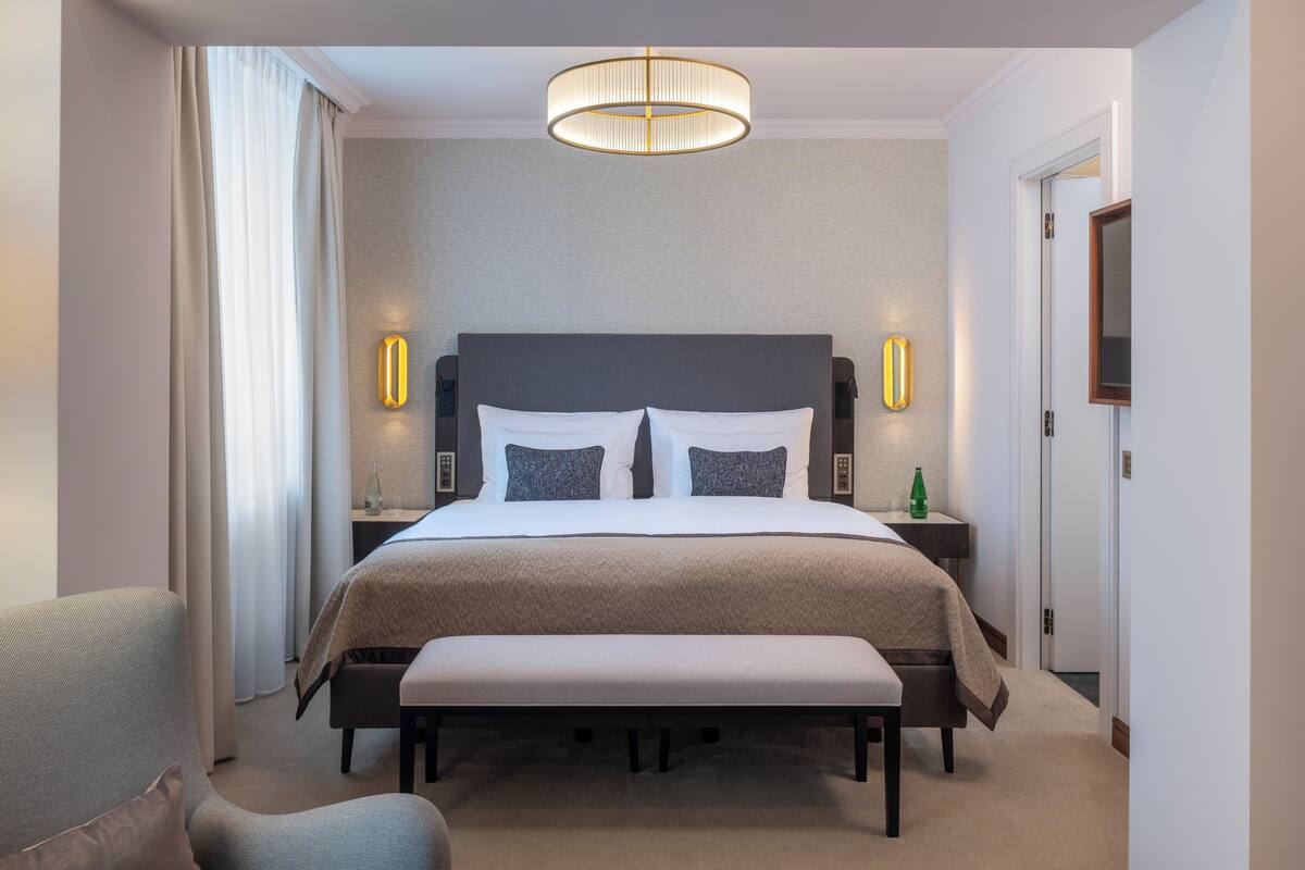 Una habitación de hotel con una cama grande, mesitas de noche, un banco y una lámpara colgante.