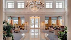 A grand lobby with a high ceiling, ornate chandelier, and a central seating area with sofas and armchairs.