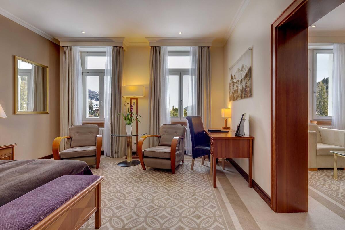 Habitación de hotel con una cama grande, dos sillones, un escritorio y vistas al exterior.