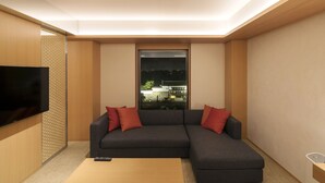 Un salon moderne avec un canapé d’angle, un téléviseur à écran plat et une fenêtre donnant sur des immeubles.