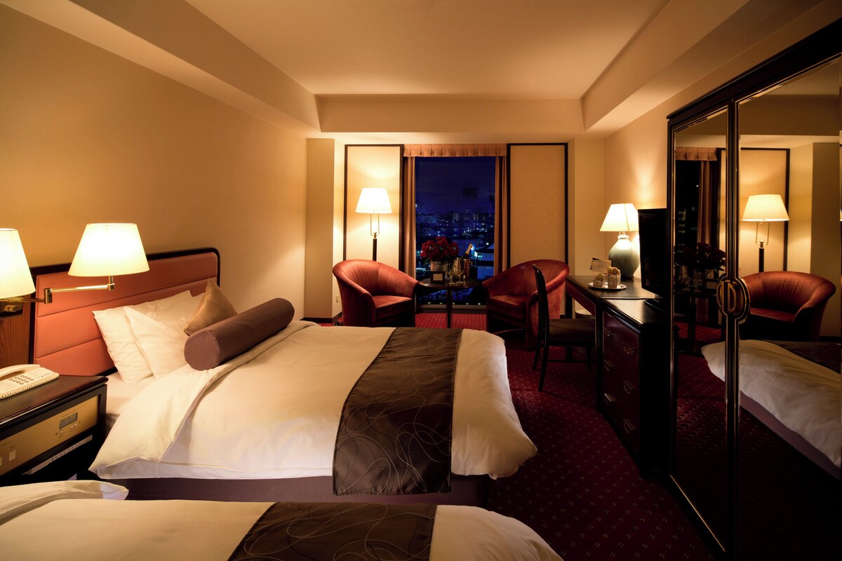 Une chambre d’hôtel avec un lit, deux chaises, un bureau et un grand miroir.
