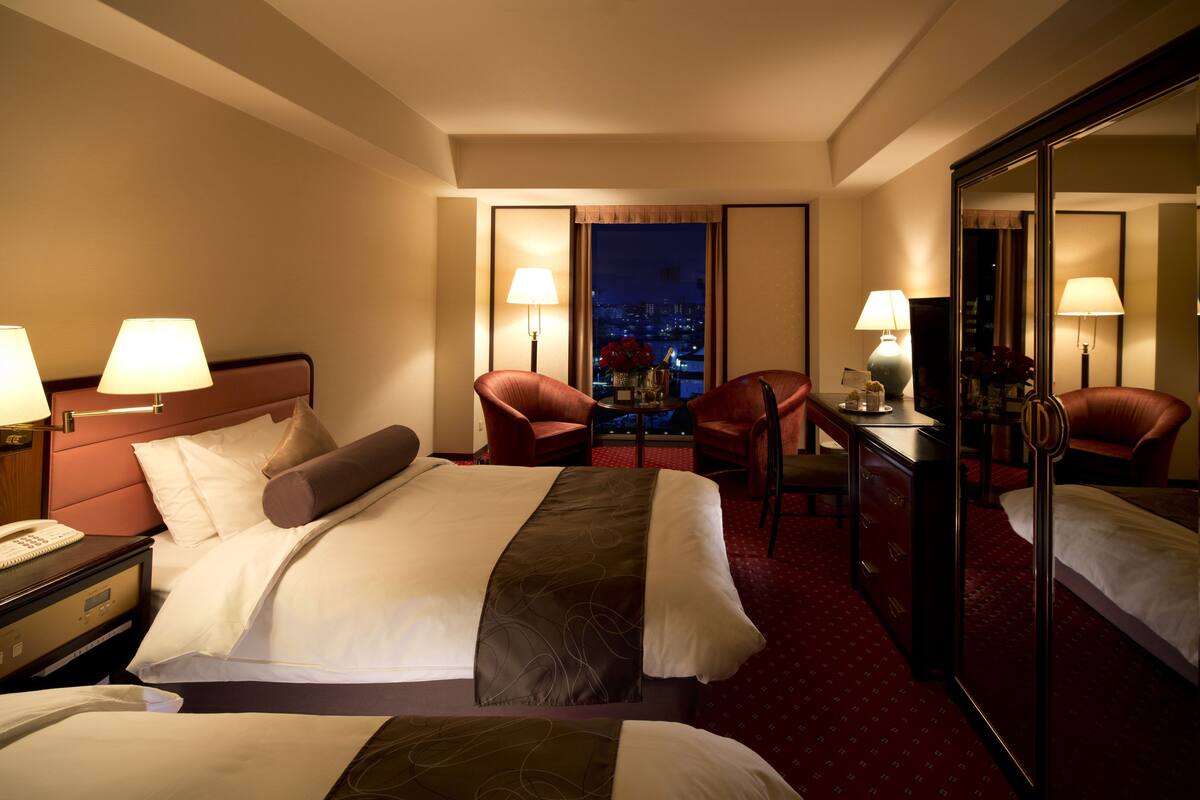 A hotel room with a large bed, two armchairs, a desk, and a mirror.