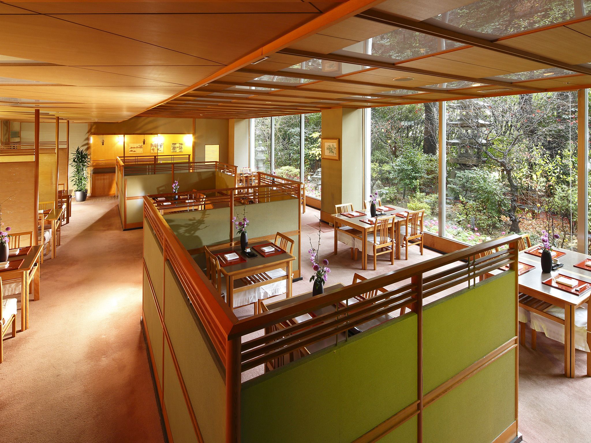 Een traditioneel Japans restaurant met tatami vloermatten, houten tafels en uitzicht op de omliggende bomen.