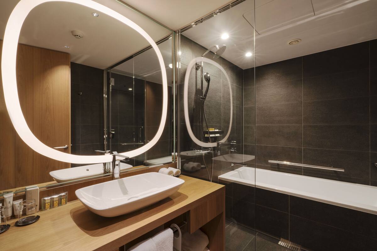 A modern bathroom with a wooden vanity, a large mirror, a bathtub, and a shower area.