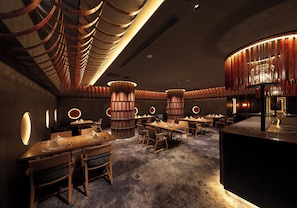 Un interior de restaurante con varias mesas, sillas y una columna decorativa central.