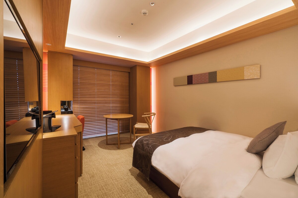 Une chambre d’hôtel avec un lit, un bureau et une chaise, une petite table et un grand miroir.