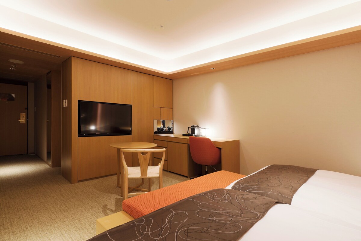 Une chambre d’hôtel équipée d’un lit, d’un bureau, d’une chaise, d’une télévision et d’une machine à café.