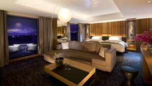 Een moderne hotelkamer met een groot bed, een bank, een bijzettafeltje en uitzicht op de stad 's nachts.